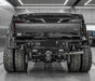 Rear view of a black Ford Platinum 3500 Super Duty truck with a heavy-duty custom rear bumper, dual rear tires, and off-road tires in a garage setting.