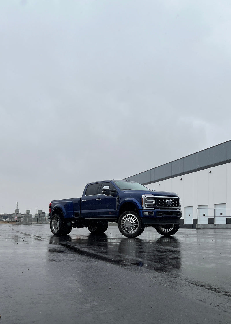 Blue pickup truck on a wet concrete surface with a building in the background