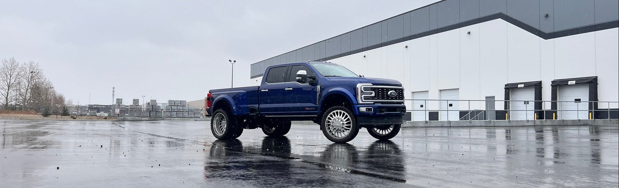 Blue pickup truck parked in a wet parking lot with a building in the background